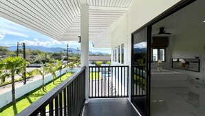 Varanda com vista para uma piscina e vegetação, um quarto moderno com cama e mesa de cabeceira, e uma parede exterior branca.