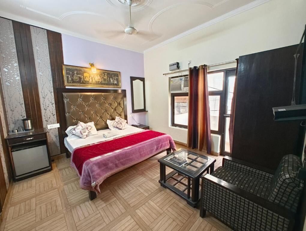 Une chambre d’hôtel avec un lit, une petite table, une chaise, une armoire et une fenêtre avec des rideaux.