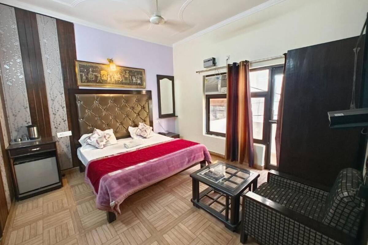 A hotel room with a bed, a small table, a chair, a wardrobe, and a window with curtains.
