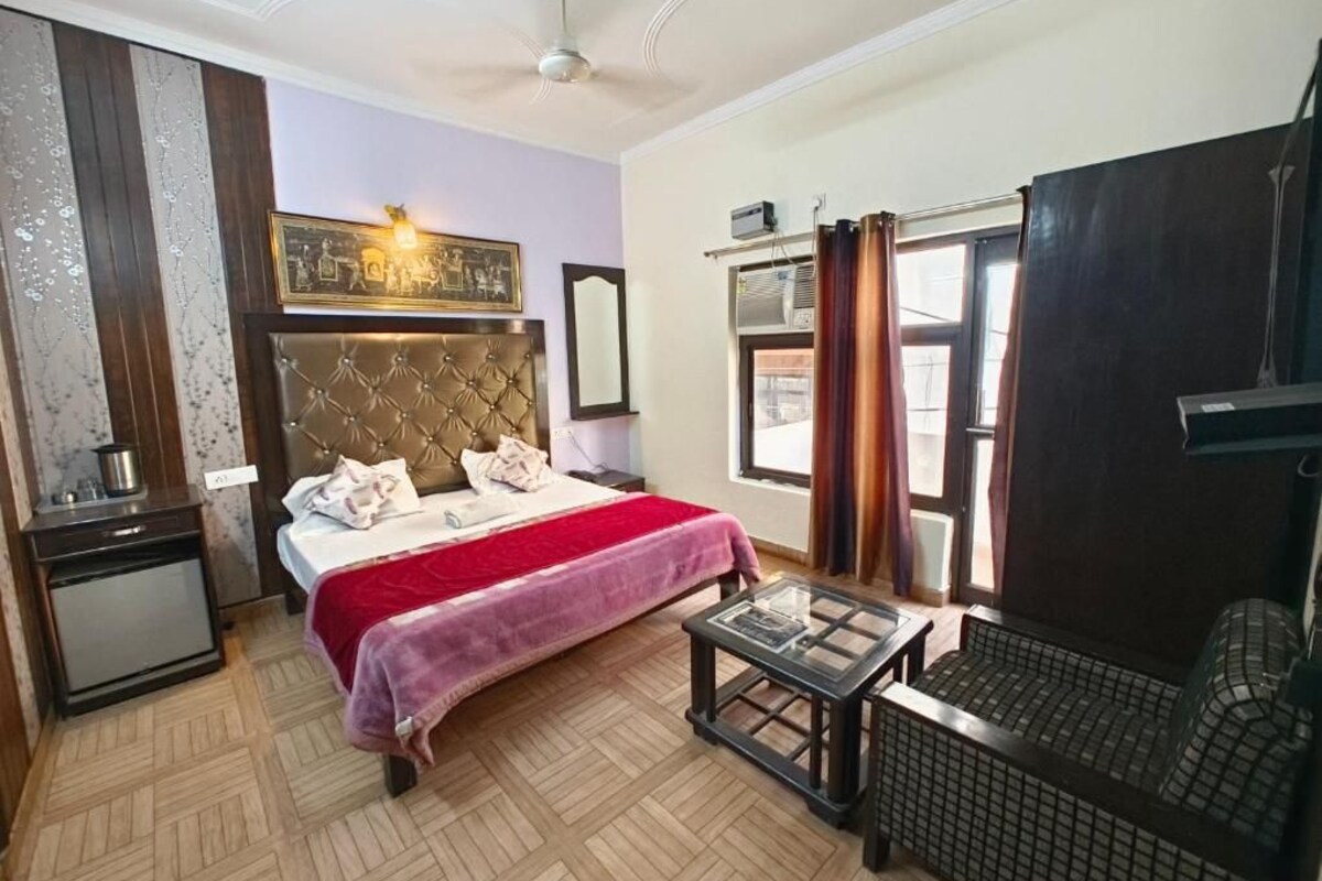A hotel room with a bed, a small table, a chair, a wardrobe, and a window with curtains.