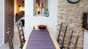 A dining area with a long wooden table, four chairs, and a stone wall with a clock. - Grand Cru (Chardonnay)