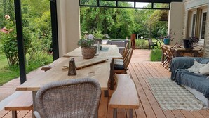A covered patio with a wooden table, wicker chairs, a sofa, and potted plants. - Grand Cru (Chardonnay)