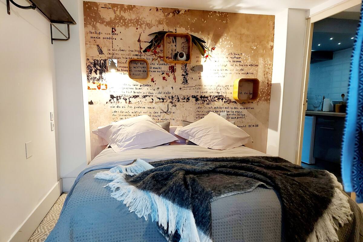 A bedroom with a bed, pillows, a blanket, and a wall with text and decorations.