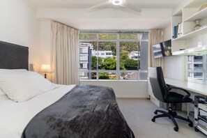 Hotelkamer met een bed, een bureau, een stoel, een televisie en een raam met uitzicht op gebouwen en bomen.