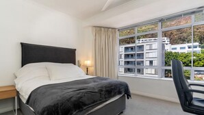 Ein modernes Hotelzimmer mit großem Fenster, einem Bett, einem Schreibtisch und einem Stuhl.