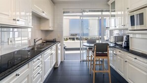 A modern kitchen with white cabinets, a black countertop, and a dining area with a table and chairs. - Cozy 2 Bedroom Beachfront Apartment (Cape Town)