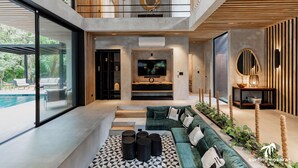 A modern living room with a large TV, a green sofa, and a pool visible through the glass doors. - La Bandida luxury villa Guiones (Nosara)