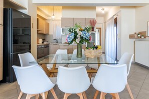 A modern kitchen with a glass dining table, white chairs, and a vase of flowers.