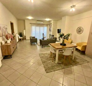A spacious living area with a dining table, sofas, and a TV. - Zephyrus Cityscape Condo, Apartment (Heraklion)