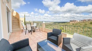 A balcony with wicker furniture, a table, and chairs, overlooking a hilly landscape. - Villa Nosredna 5 Bedroom & Pool LES01 (Ayamonte)