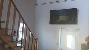 Una escalera con barandillas de madera, un cuadro en la pared, una puerta con un ventanal y una cesta en el suelo.