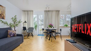 A modern living room with a sofa, dining table, chairs, a TV, and a large window with curtains. - Lumina spacious apartment in Warsaw (Warsaw)