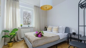 A modern bedroom with a bed, bedside table, chair, potted plant, and a window with curtains. - Lumina spacious apartment in Warsaw (Warsaw)