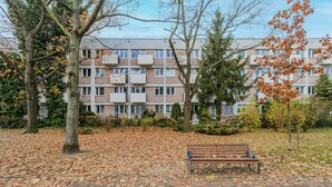 A park with a bench and trees, surrounded by a multi-story building with balconies. - Lumina spacious apartment in Warsaw (Warsaw)