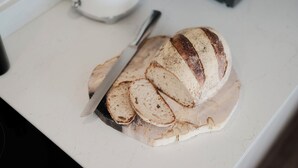 Une miche de pain tranché sur une planche à découper blanche, avec un couteau à côté.
