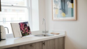 Une cuisine avec un plan de travail blanc, un évier en acier inoxydable, des armoires en bois et un tableau encadré accroché au mur.