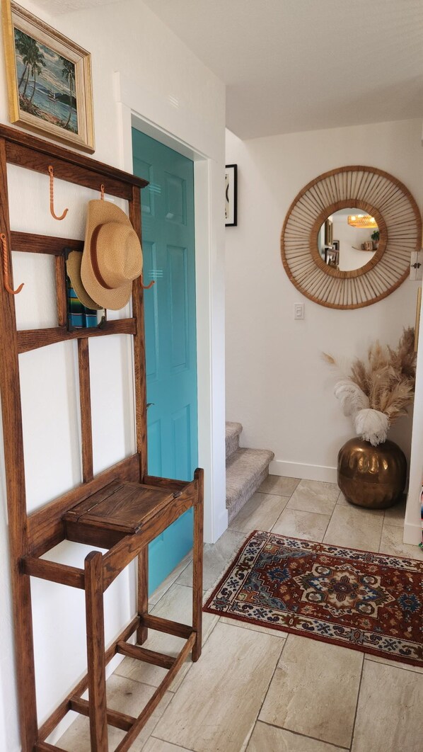 A hallway with a wooden chair, a blue door, a mirror, and a patterned rug.