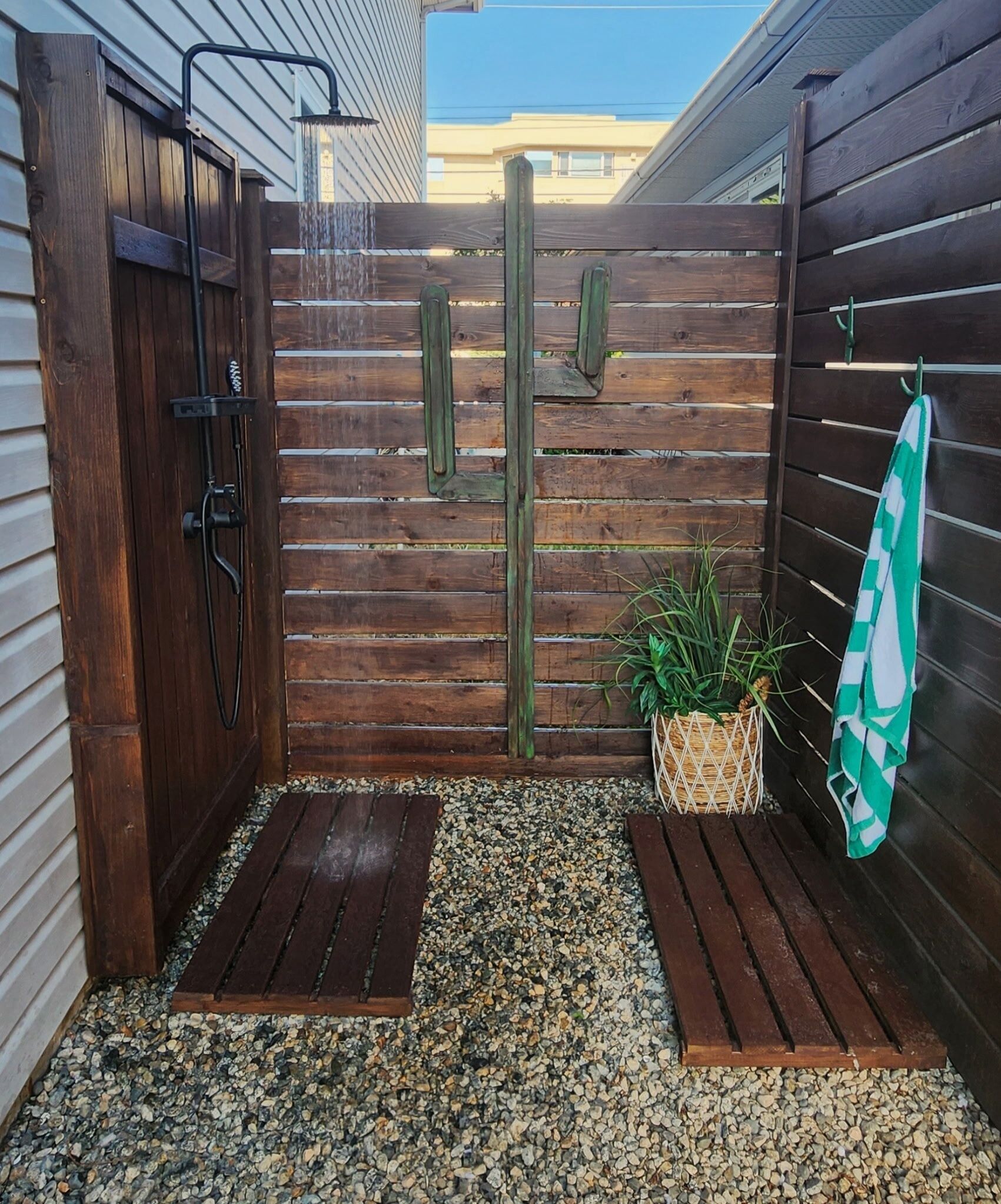 A wooden shower enclosure with a rain showerhead, a small potted plant, and a towel hanging on a rack.