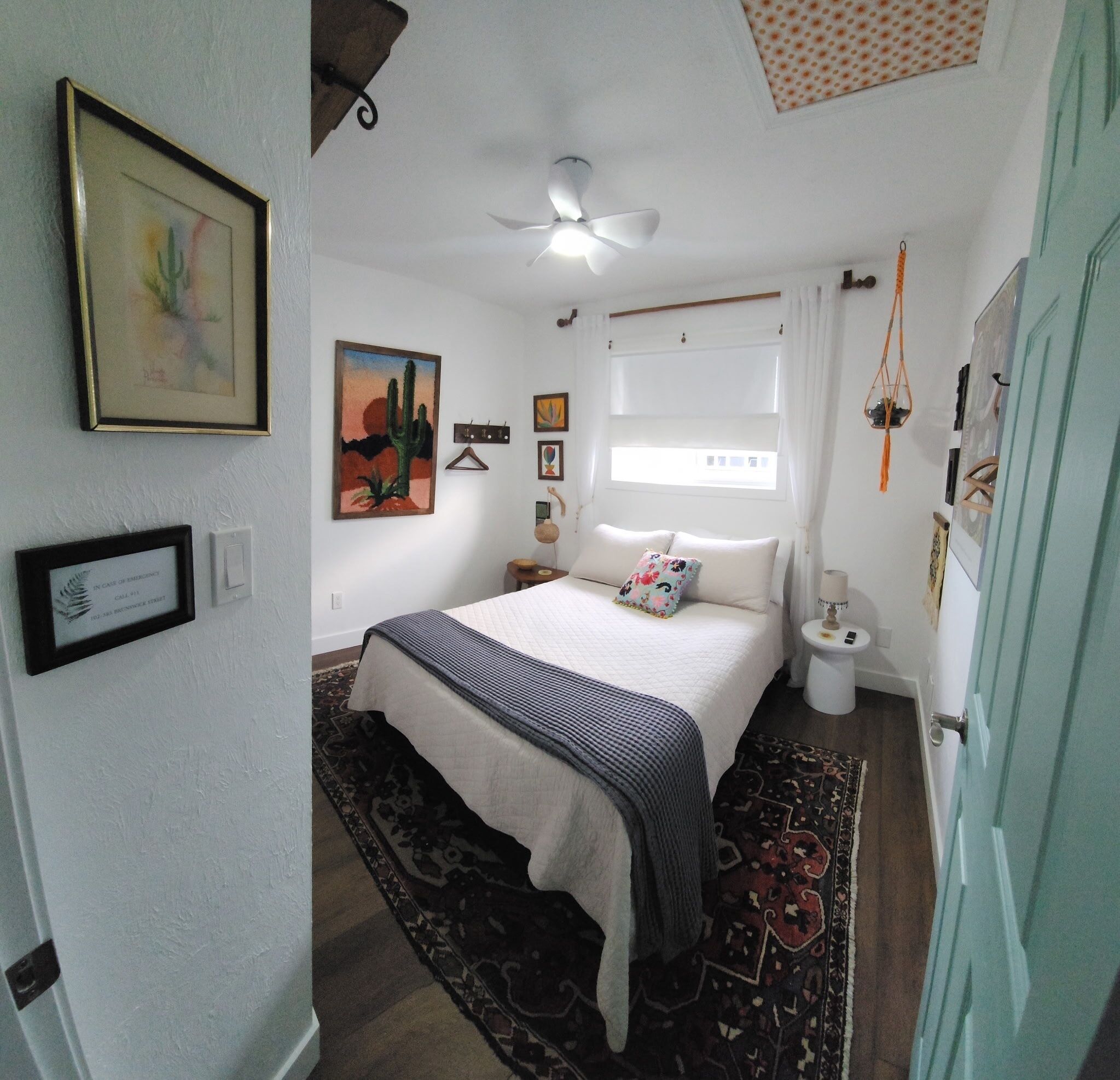 Een slaapkamer met een bed, plafondventilator, raam met gordijnen en een deur.