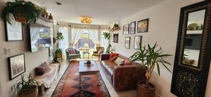 Una sala de estar acogedora con un sofá, un sillón y una mesa de centro, decorada con plantas y cuadros enmarcados.