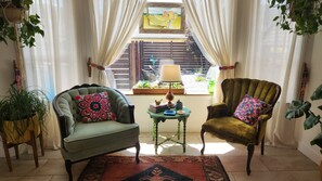 Una habitación con dos sillones, una mesita con lámpara y vista a un jardín a través de un ventanal.