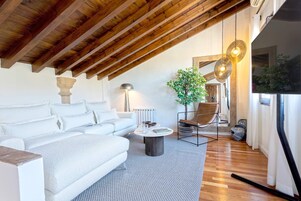 A modern living room with a high ceiling, wooden beams, a white sofa, a round coffee table, and a potted plant.