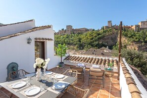 An outdoor dining area with a table set for four, overlooking a historic town with terracotta-roofed buildings and a castle on a hill. - Genteel Home Mirador de los Reyes (Granada)