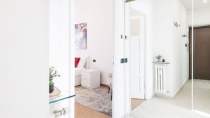 Una habitación de hotel moderna con un separador de vidrio, una cama blanca, una mesita pequeña y un cuadro colorido en la pared.