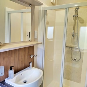 Un baño moderno con ducha de vidrio, lavamanos blanco y tocador de madera.