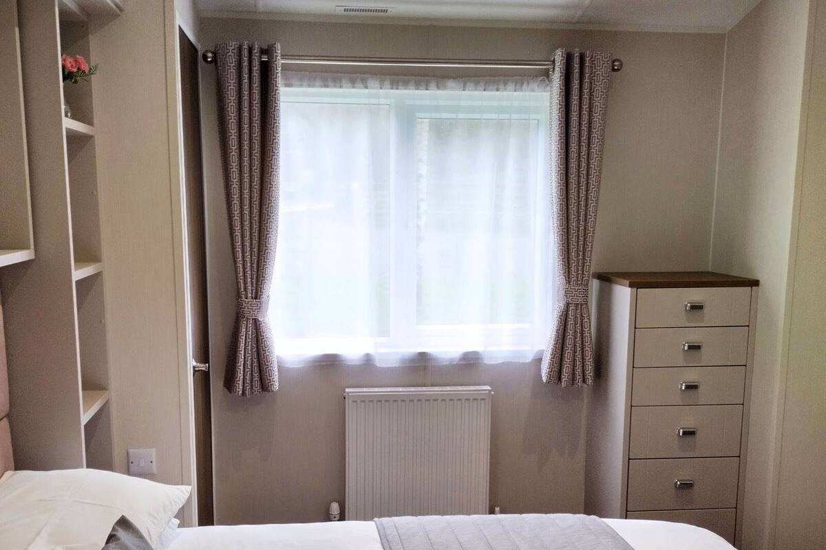 Un dormitorio con cama, cómoda, radiador y ventana con cortinas.