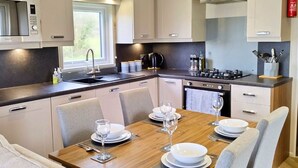 Een moderne keuken met een eethoek, met een houten tafel gedekt voor vier personen, een inbouwoven en een magnetron.