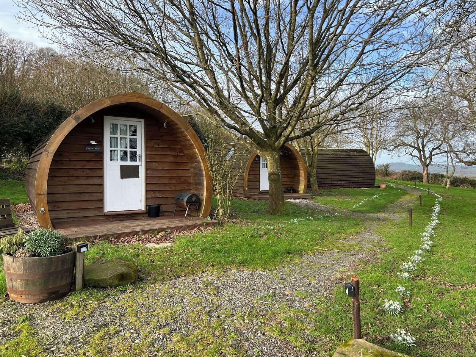 A wooden cabin with a circular archway, a door, and a small porch area with a barbecue grill.