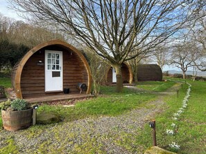 Una cabaña de madera con un arco circular, una puerta y un pequeño porche con una parrilla.