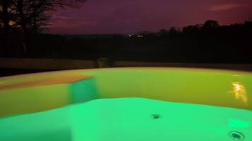 A hot tub with a green light, surrounded by a dark landscape and a purple sky.