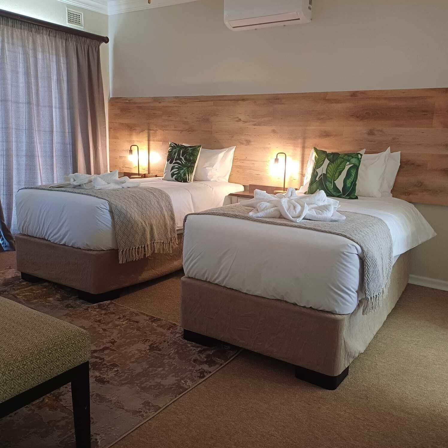 A hotel room with two beds, each with a headboard, bedside lamps, and a wooden headboard.