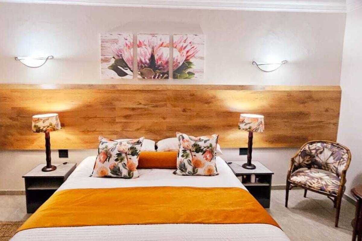 A bedroom with a wooden headboard, two bedside lamps, a floral bedspread, and a chair.