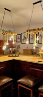 Un rincón de bar con taburetes de madera, una escultura de caballo y una lámpara con luces de cuerda.