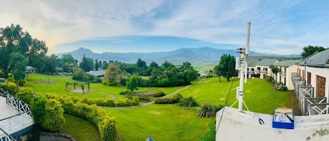 Vista panorámica de un hotel con un paisaje verde exuberante, una cadena montañosa al fondo y cielo despejado.