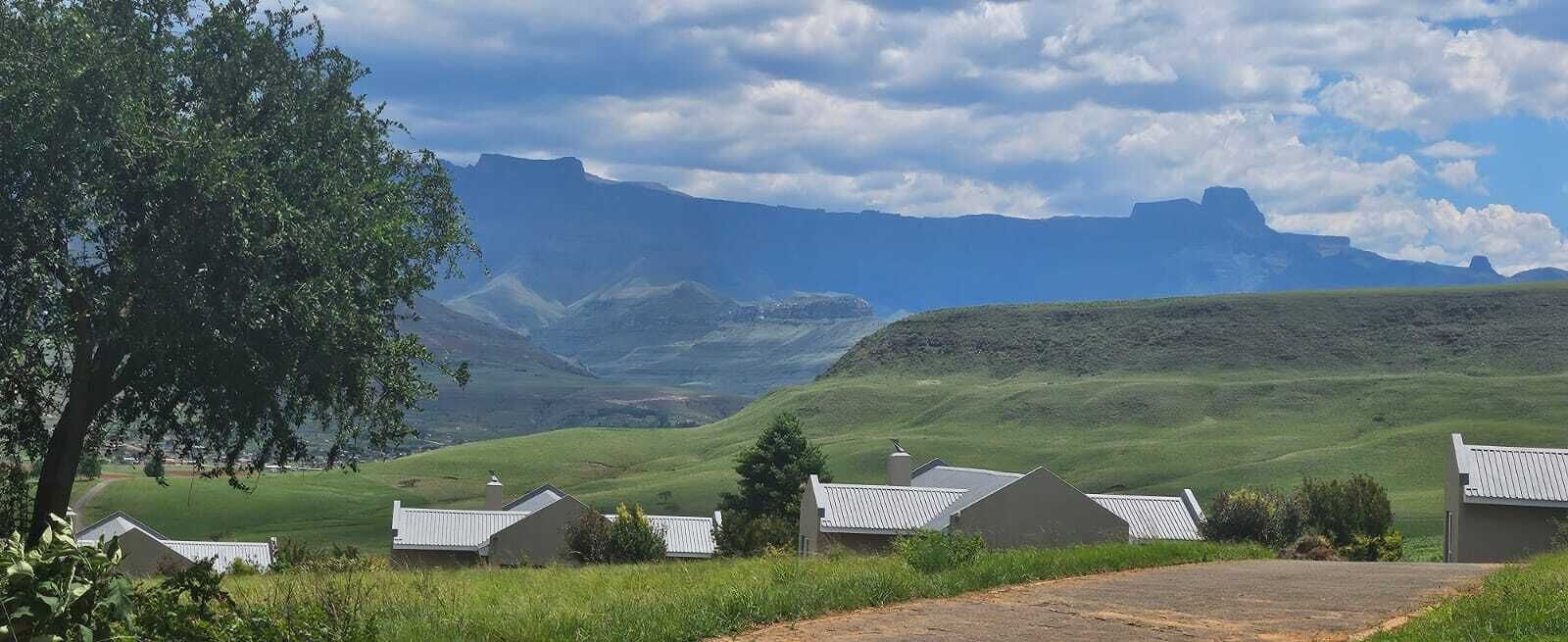 A rural landscape with houses, a tree, and mountains in the background.