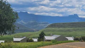 A rural landscape with houses, a tree, and mountains in the background.