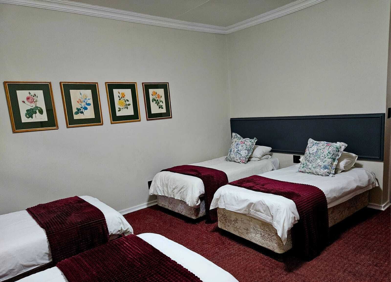Habitación de hotel con dos camas, un cabecero oscuro y tres láminas botánicas enmarcadas en la pared.