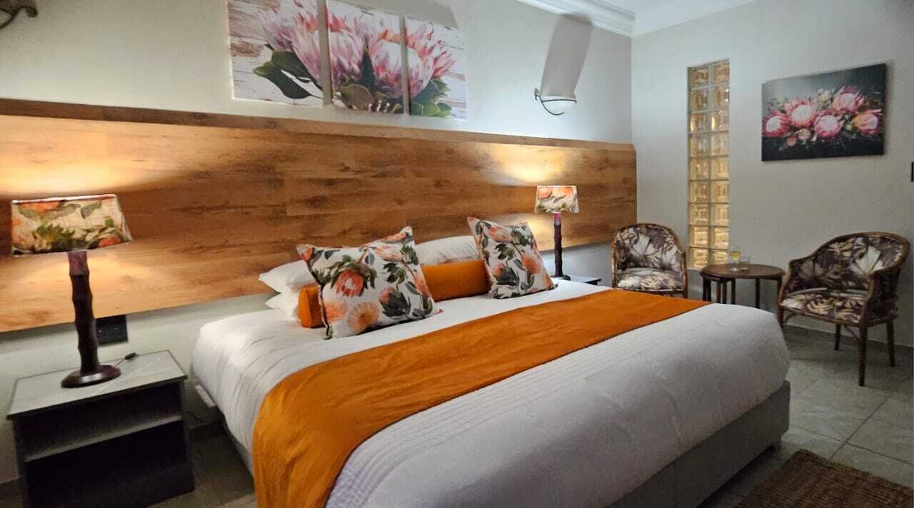 A bedroom with a large bed, two bedside tables, a nightstand, a wooden headboard, and floral artwork on the walls.