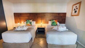 Une chambre d’hôtel avec deux lits, une tête de lit en bois, du linge de lit blanc et une estampe botanique encadrée au mur.