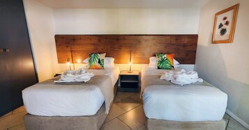 Habitación de hotel con dos camas, cabecero de madera, ropa de cama blanca e impresión botánica enmarcada en la pared.