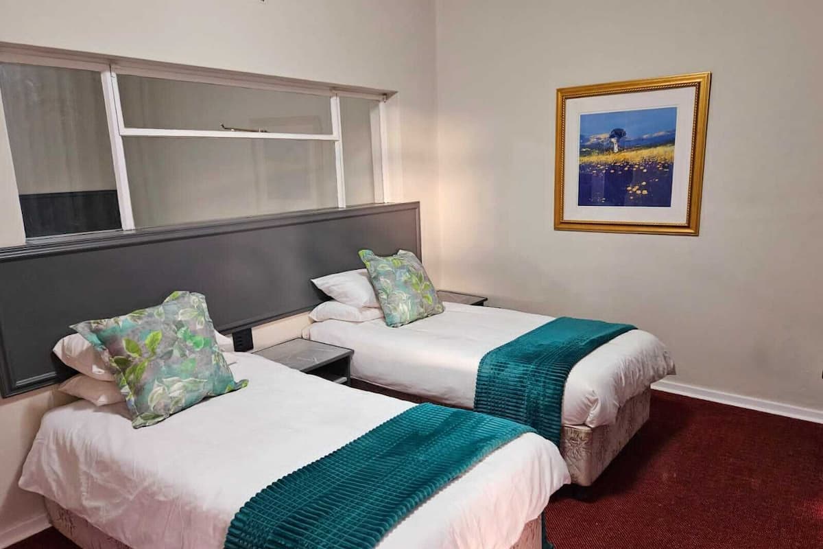 A hotel room with two single beds, a nightstand, a window, and a framed picture on the wall.