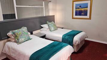 Habitación de hotel con dos camas individuales, una mesita de noche, una ventana y un cuadro enmarcado en la pared.