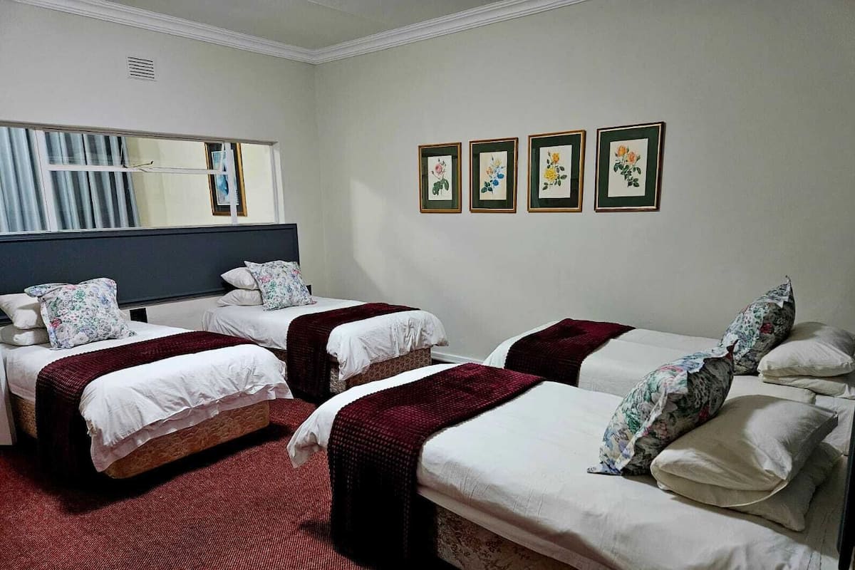 A hotel room with three single beds, a large mirror, and three framed floral paintings on the wall.