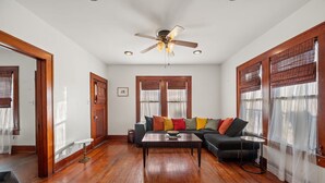 A living room with hardwood flooring, a ceiling fan, a sofa with colorful cushions, a coffee table, and a small side table. - The Yellow Rose of SoCo:Charming Home Steps from South Congress and 1 mile to Downtown (Austin)