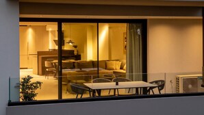 A modern living room with a sofa, dining table, and chairs, visible through a glass partition. - RiverSide Villas Kalamata B1 (Kalamata)