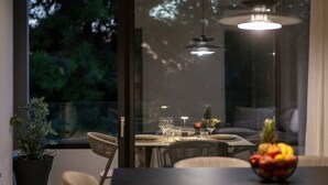 A dining area with a table set for two, a potted plant, and a fruit bowl. - RiverSide Villas Kalamata C2 (Kalamata)